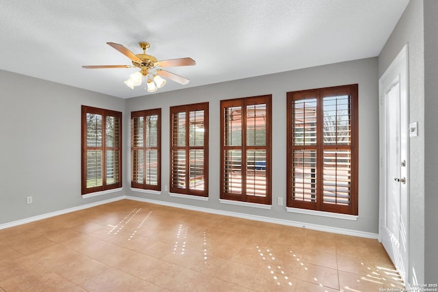 empty room featuring light tile patterned floors, ceiling fan, baseboards, and a textured ceiling