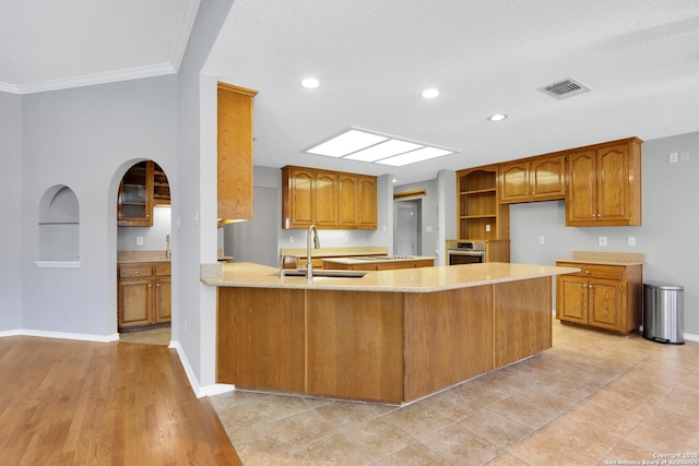 kitchen featuring stainless steel oven, brown cabinets, visible vents, and a sink