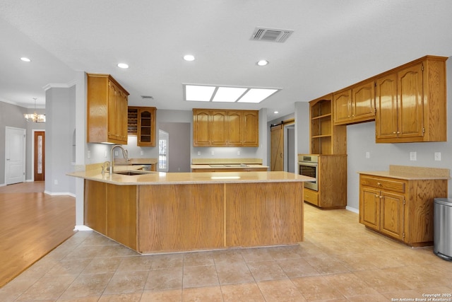 kitchen featuring a barn door, oven, a peninsula, a sink, and visible vents