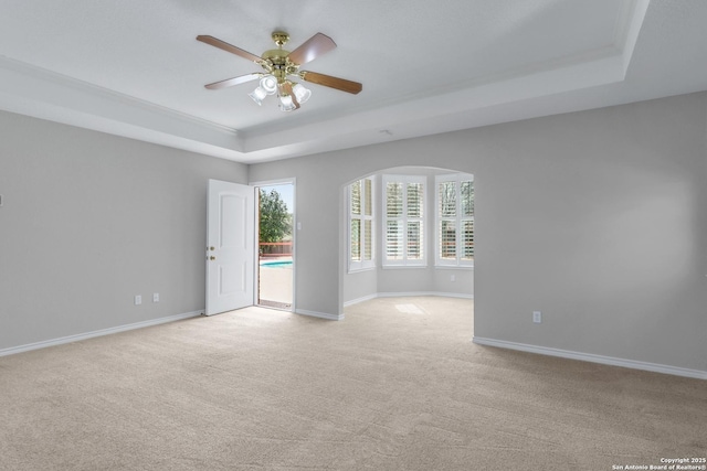 spare room featuring light carpet, baseboards, a tray ceiling, and ceiling fan