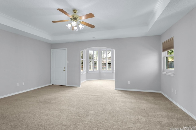 unfurnished room featuring light carpet, a tray ceiling, arched walkways, and baseboards