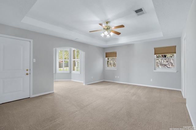 empty room featuring a raised ceiling, light colored carpet, visible vents, a ceiling fan, and baseboards