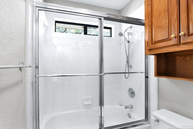 bathroom with a textured wall, shower / bath combination with glass door, and toilet