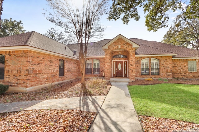 view of front of property with a shingled roof, brick siding, and a front lawn