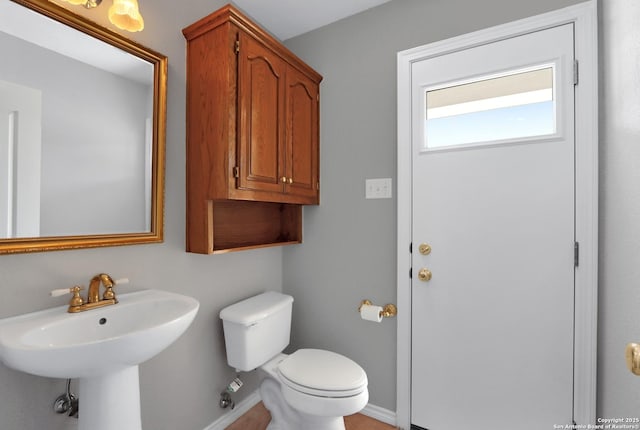 half bathroom with baseboards, a sink, and toilet