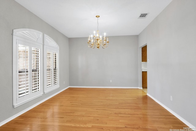 spare room with visible vents, light wood-style flooring, baseboards, and an inviting chandelier