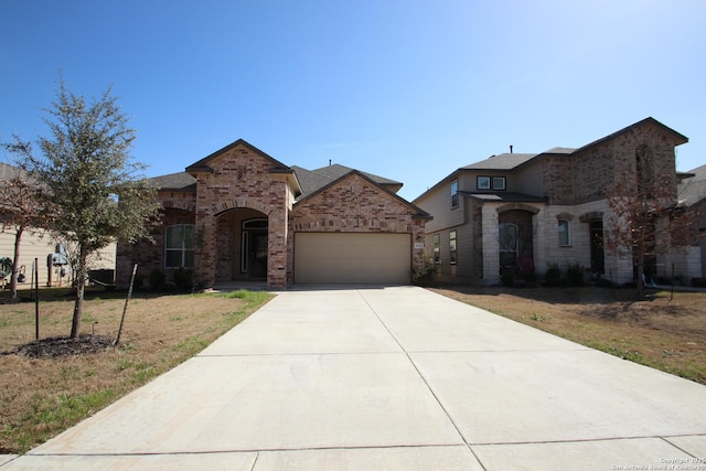 french country home featuring an attached garage, a front yard, concrete driveway, and brick siding