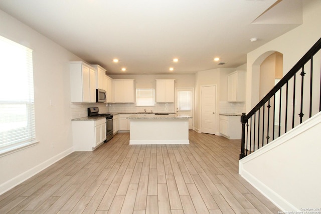 kitchen featuring stainless steel appliances, a kitchen island, light wood finished floors, and tasteful backsplash