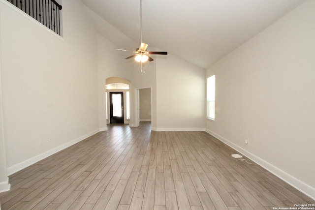 unfurnished living room with a ceiling fan, arched walkways, baseboards, and light wood finished floors