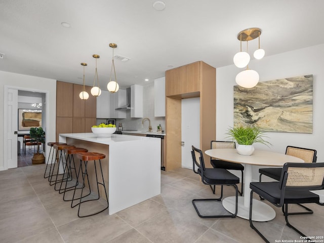 kitchen with modern cabinets, a breakfast bar, a center island, light countertops, and wall chimney range hood