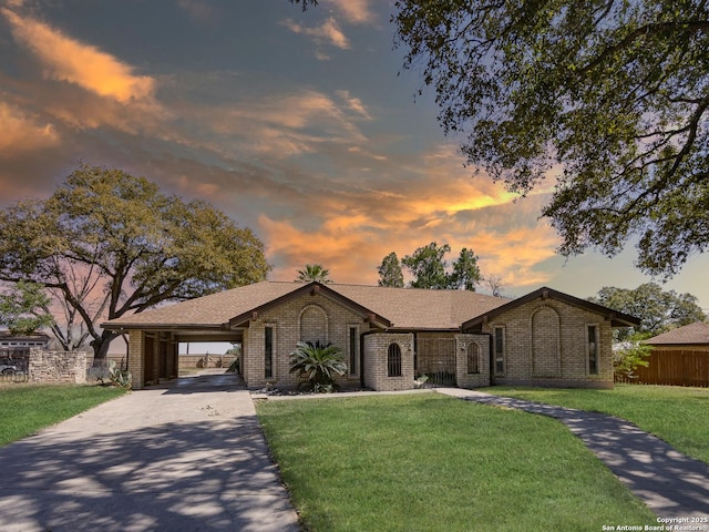 view of front facade featuring brick siding, a front yard, fence, an attached carport, and driveway