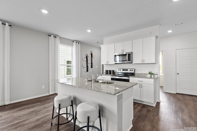 kitchen with stainless steel appliances, dark wood-type flooring, white cabinets, a kitchen island with sink, and a sink