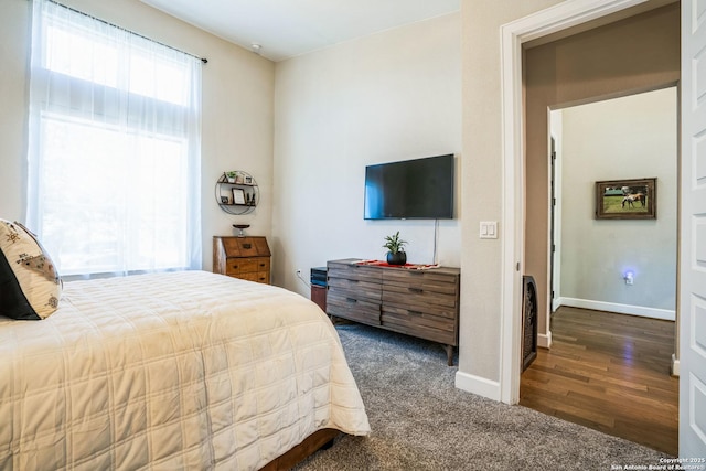 bedroom with dark colored carpet, dark wood-style flooring, and baseboards