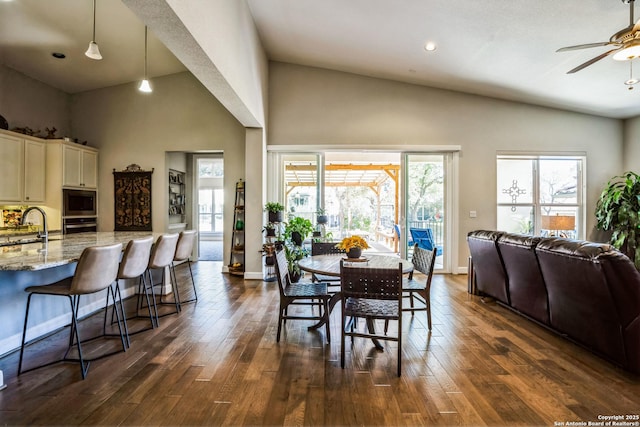 dining area featuring high vaulted ceiling, dark wood-style flooring, a ceiling fan, and baseboards