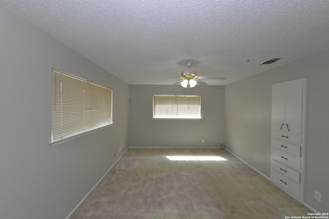 unfurnished room with ceiling fan, a textured ceiling, light carpet, visible vents, and baseboards