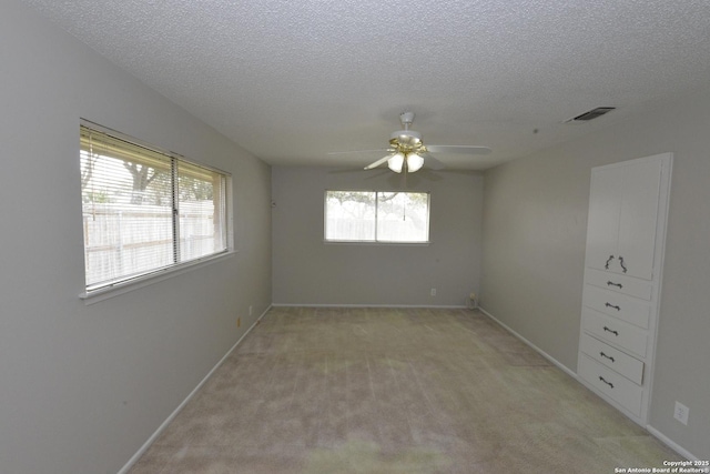 unfurnished room featuring light carpet, a ceiling fan, visible vents, and a textured ceiling