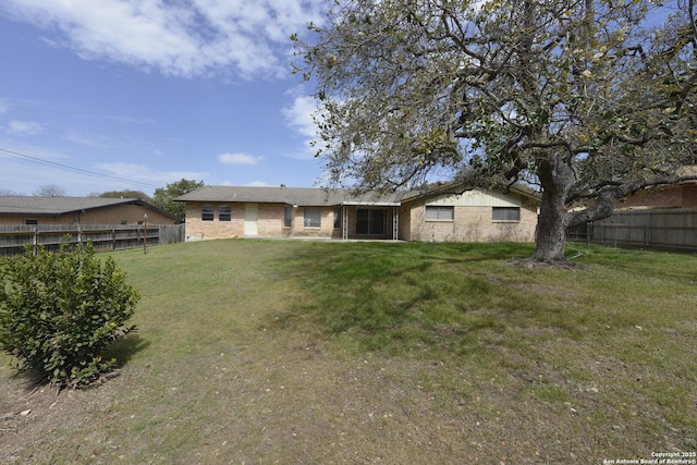 rear view of property featuring brick siding, fence, and a yard