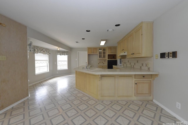 kitchen with under cabinet range hood, light brown cabinets, visible vents, and a sink