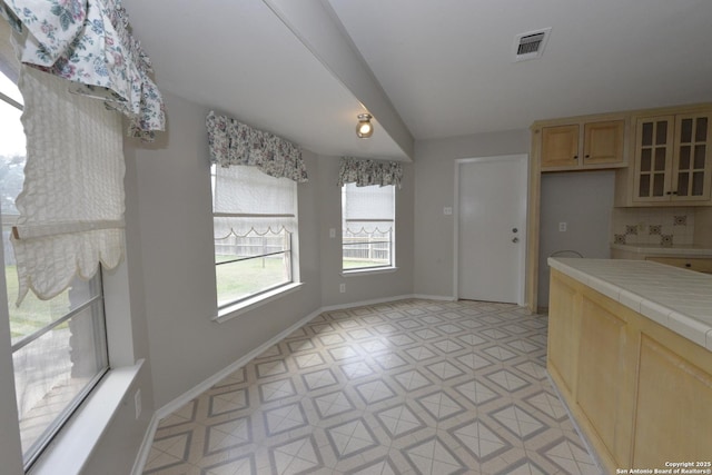 kitchen featuring tile counters, light brown cabinetry, visible vents, and baseboards