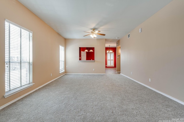 empty room with ceiling fan with notable chandelier, carpet flooring, a wealth of natural light, and baseboards