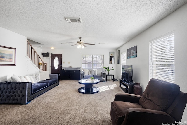 carpeted living room featuring visible vents, stairway, ceiling fan, and a textured ceiling