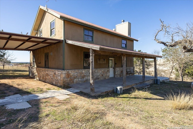 rear view of house featuring stone siding, a carport, a patio, and a chimney