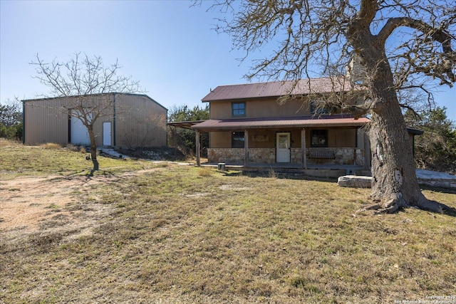 rear view of house with stone siding, covered porch, a lawn, and an outbuilding