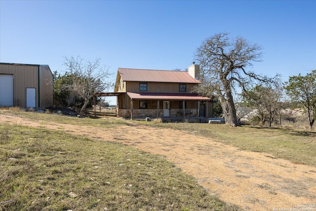 back of house featuring a chimney, a porch, a lawn, metal roof, and stone siding