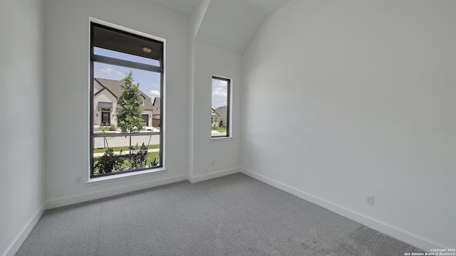 carpeted spare room with plenty of natural light, baseboards, and lofted ceiling