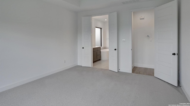 unfurnished bedroom featuring light carpet, baseboards, and ensuite bath