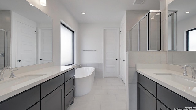 full bathroom with a shower stall, a freestanding bath, tile patterned floors, two vanities, and recessed lighting