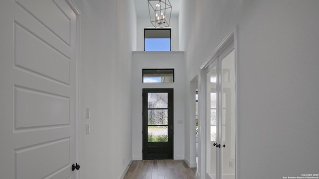 foyer entrance with baseboards, light wood-type flooring, a chandelier, and a high ceiling