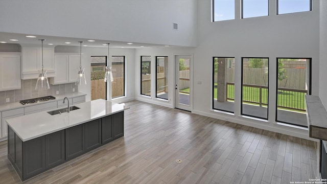 kitchen with a sink, stainless steel gas stovetop, light countertops, a high ceiling, and white cabinetry