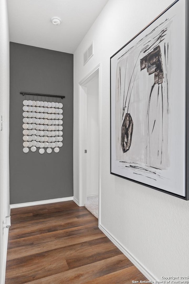 hall with wood finished floors, visible vents, and baseboards