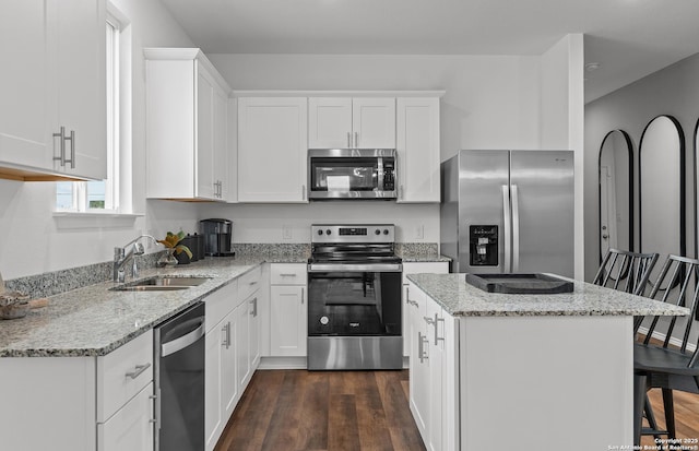 kitchen featuring dark wood finished floors, appliances with stainless steel finishes, a sink, a kitchen island, and a kitchen bar