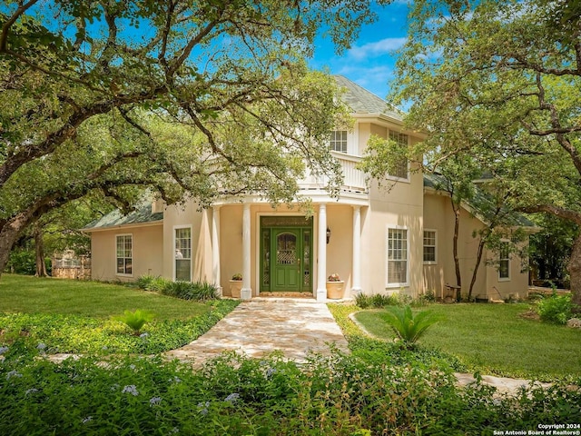 view of front of house with a front yard, a balcony, and stucco siding