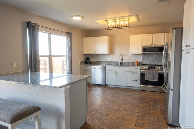 kitchen featuring stainless steel appliances, white cabinets, a sink, and light stone countertops