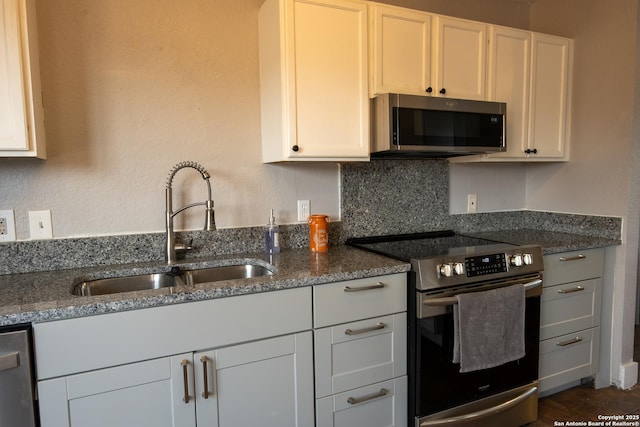 kitchen featuring tasteful backsplash, white cabinets, dark stone counters, stainless steel appliances, and a sink