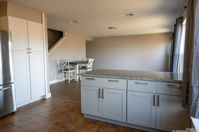 kitchen with a peninsula, visible vents, white cabinets, freestanding refrigerator, and light stone countertops