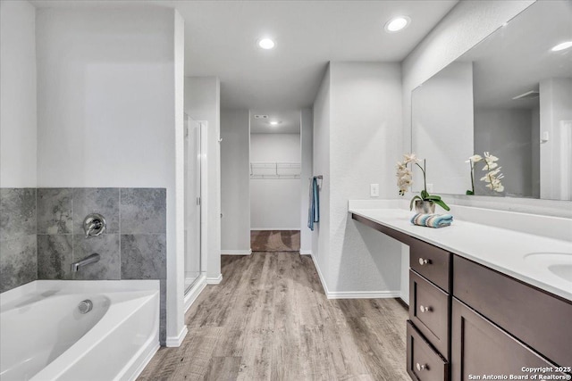 bathroom with baseboards, wood finished floors, a garden tub, a spacious closet, and vanity