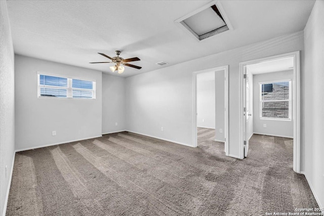 carpeted spare room with ceiling fan, visible vents, attic access, and baseboards