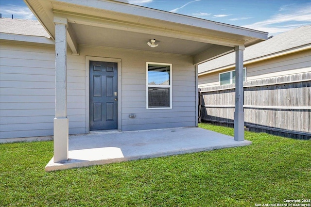 view of exterior entry featuring a lawn, a patio, and fence