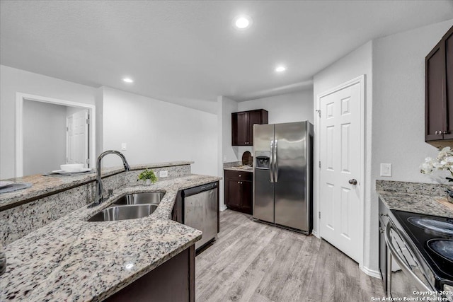 kitchen with appliances with stainless steel finishes, light wood-style floors, a sink, dark brown cabinetry, and light stone countertops