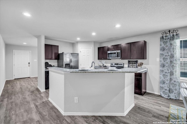 kitchen featuring an island with sink, appliances with stainless steel finishes, dark brown cabinets, light wood-type flooring, and recessed lighting