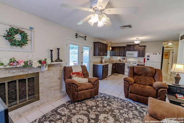 living room with light tile patterned floors, visible vents, a ceiling fan, french doors, and a fireplace