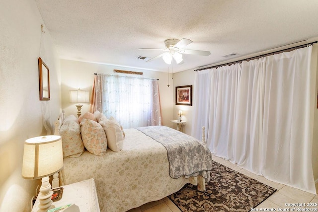 bedroom with tile patterned flooring, visible vents, ceiling fan, and a textured ceiling