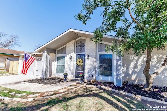 view of front of home with driveway, brick siding, an attached garage, and fence