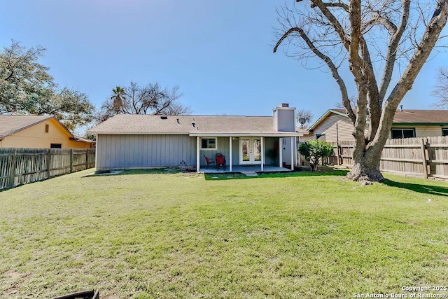 rear view of house with french doors, a patio, a fenced backyard, a chimney, and a yard