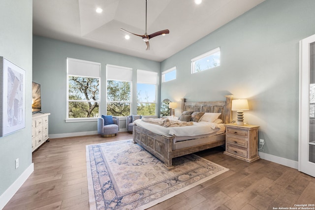 bedroom featuring a tray ceiling, recessed lighting, hardwood / wood-style floors, a high ceiling, and baseboards