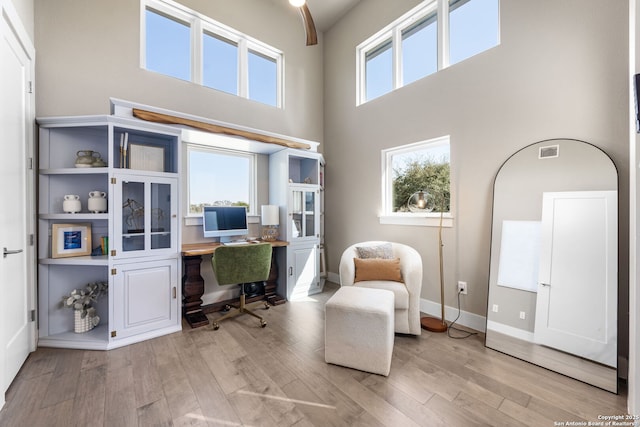 home office with light wood-type flooring, baseboards, a high ceiling, and visible vents